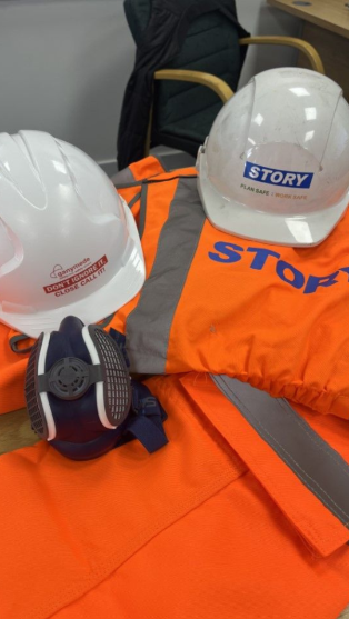 Personal protective equipment (PPE) including Story Contracting branded hard hats, high-visibility orange workwear, and a respirator mask, emphasising health and safety standards in construction and civil engineering sectors.