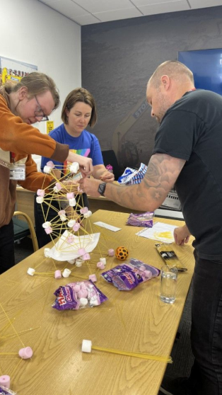 Employees engaged in a team building activity using marshmallows and spaghetti to construct towers during a corporate training workshop focused on collaboration and problem-solving skills.